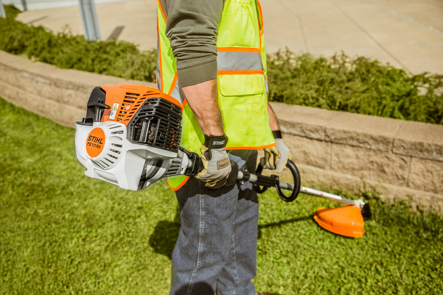 Person holding an orange and white straight shaft trimmer with loop handle for home improvement landscaping tasks