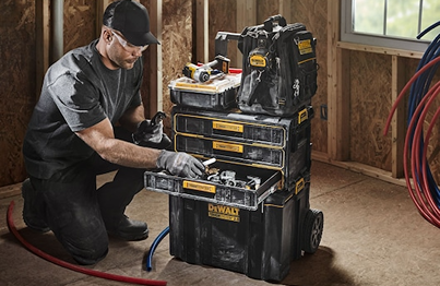 Worker organizing tools in black and yellow DEWALT ToughSystem storage unit with three drawers on jobsite