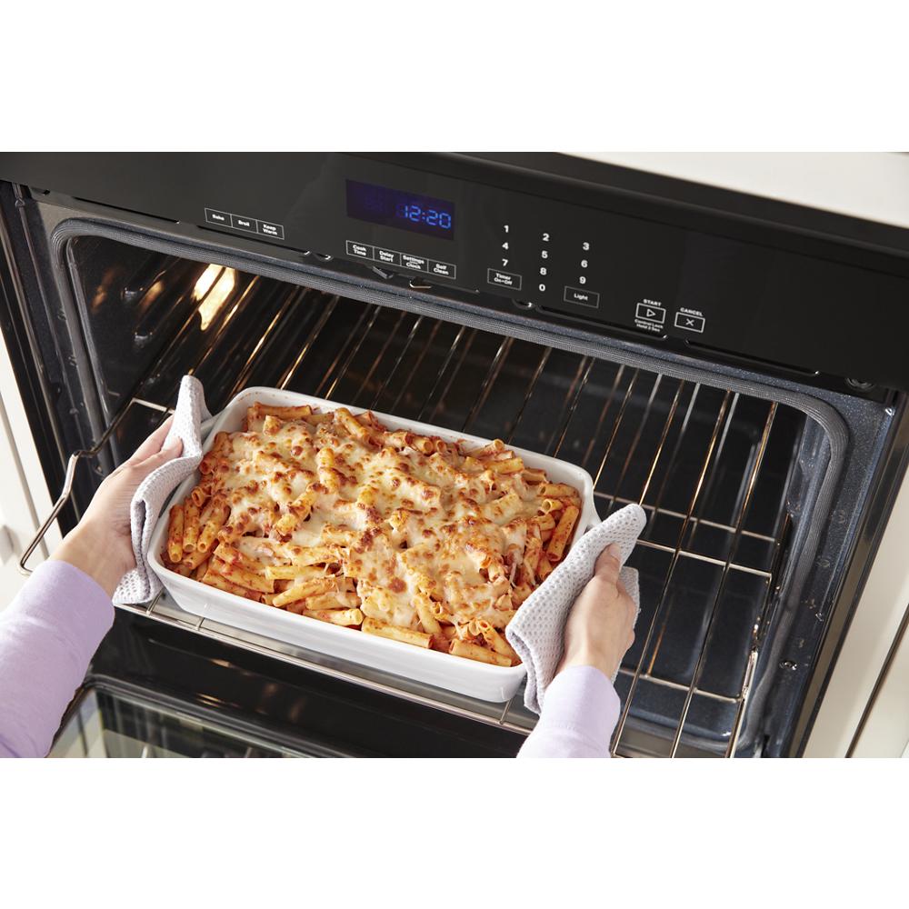 Hands removing baked pasta dish from open self-cleaning double wall oven in kitchen appliances collection