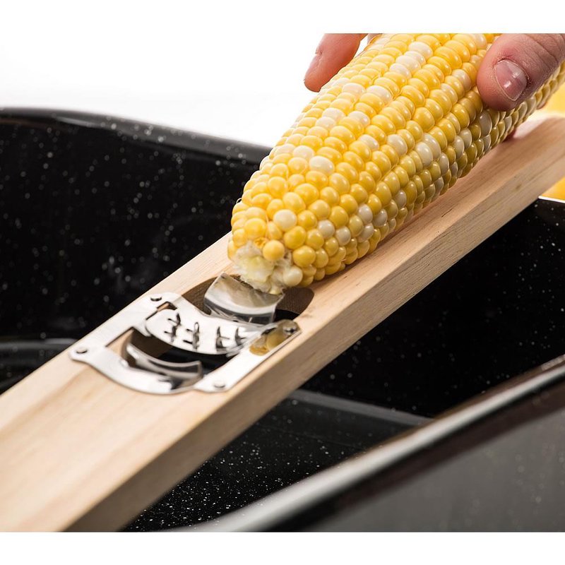 Hand using wooden corn cutter to remove kernels over black kitchenware in Kitchen Gadgets & Tools collection