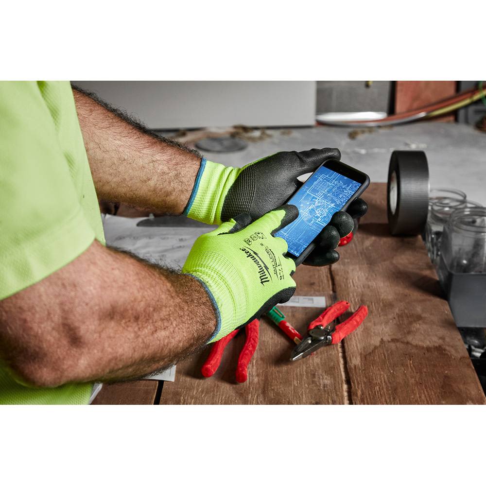 Person wearing high-visibility Milwaukee work gloves using smartphone near tools on wooden workbench for home improvement