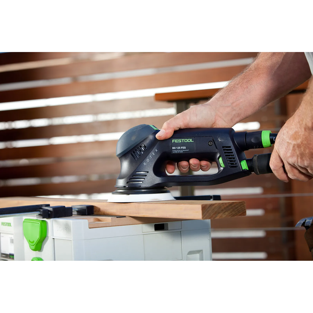 Person using Festool dual mode sander with dust extraction hose smoothing wooden plank for home improvement tool use
