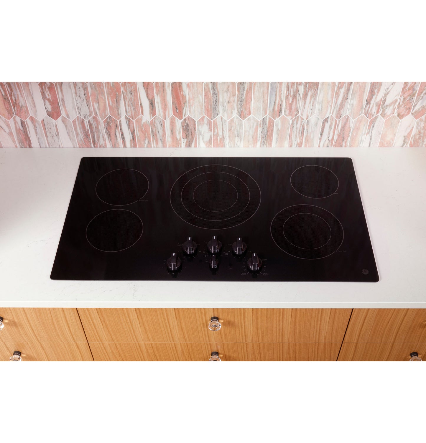 Black electric cooktop with five knob controls installed in a white countertop in a modern kitchen setting