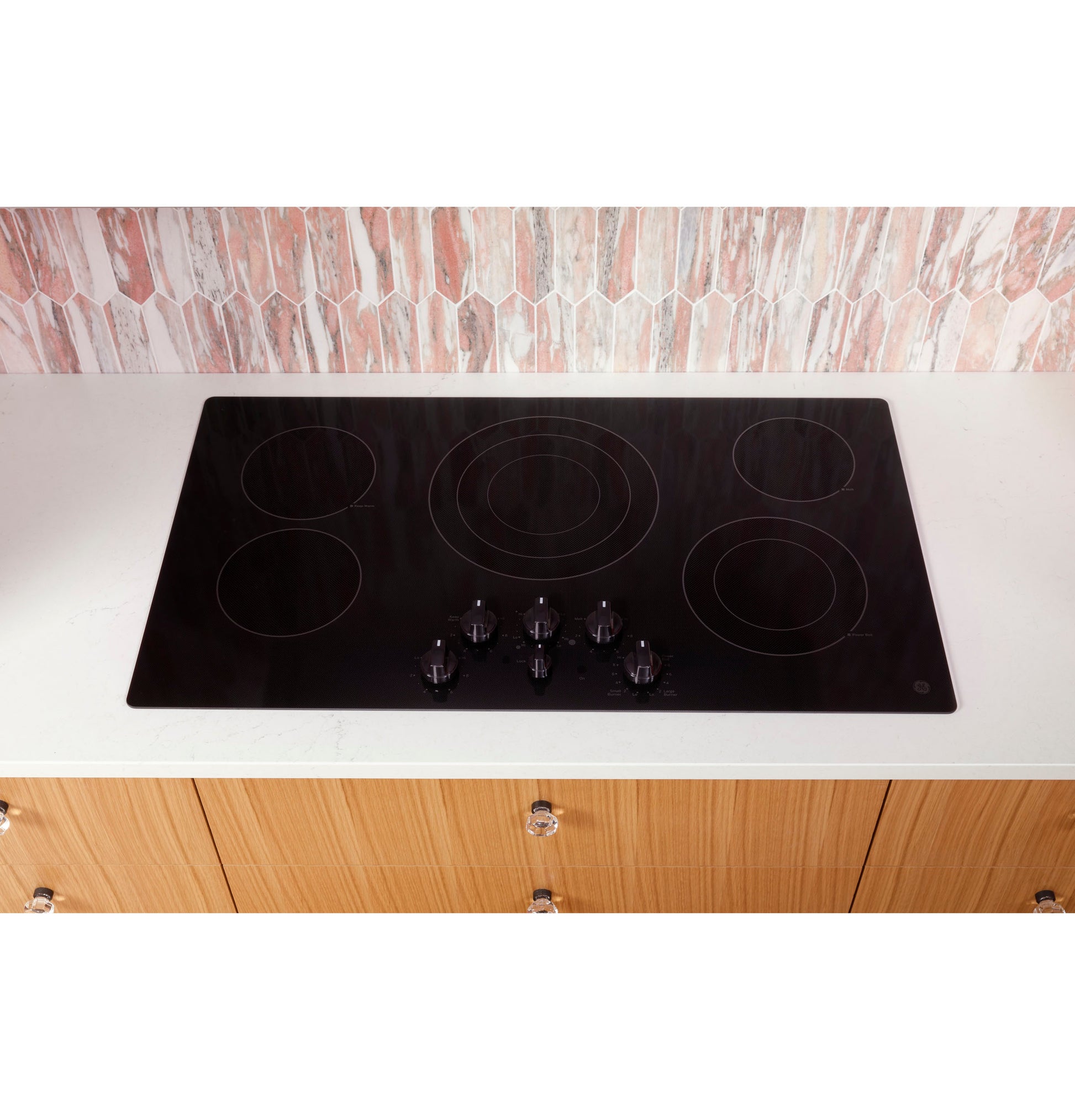 Black electric cooktop with five knob controls installed in a white countertop in a modern kitchen setting