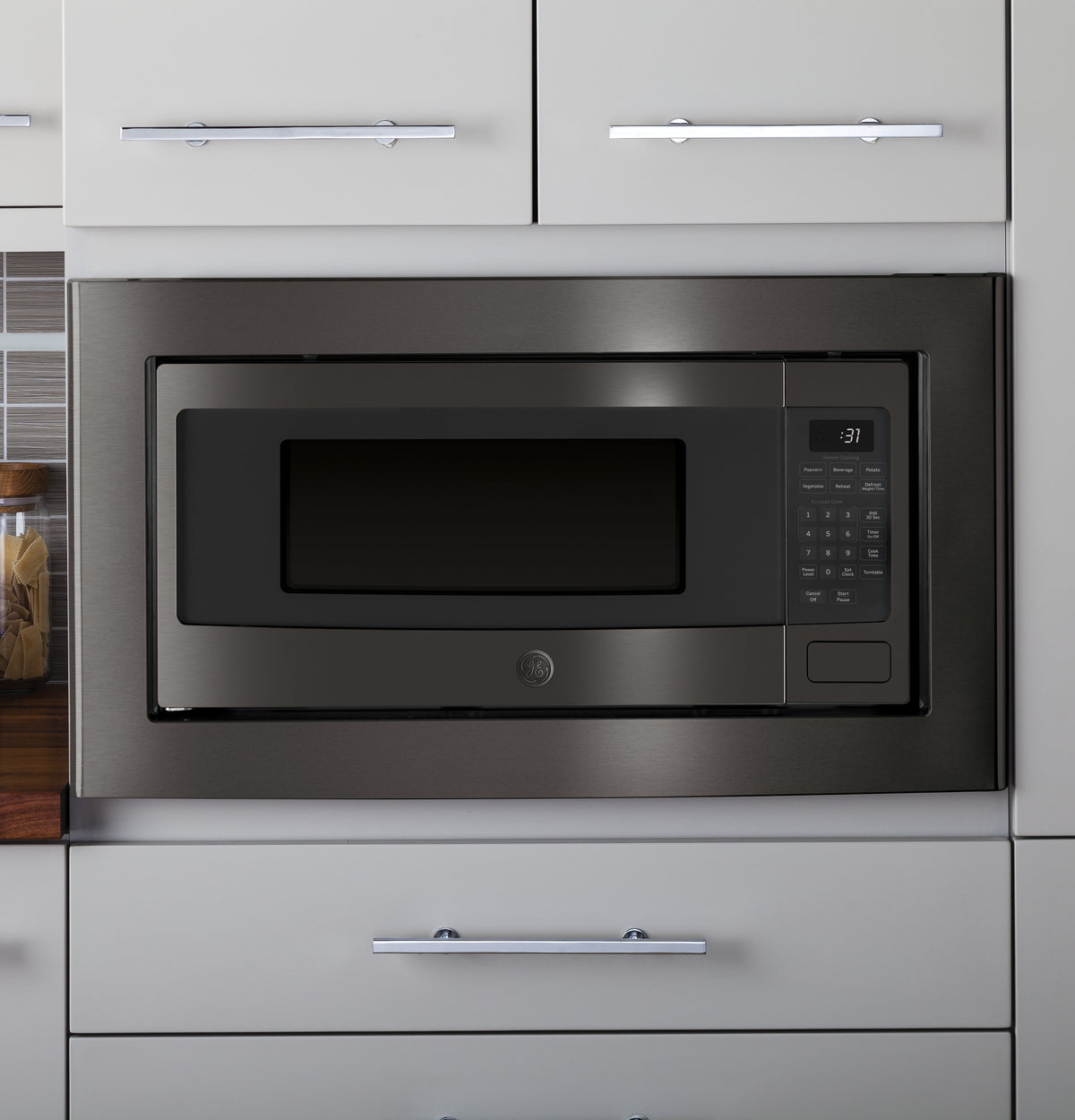 Black stainless steel built-in microwave trim kit installed within modern gray kitchen cabinetry in appliances collection