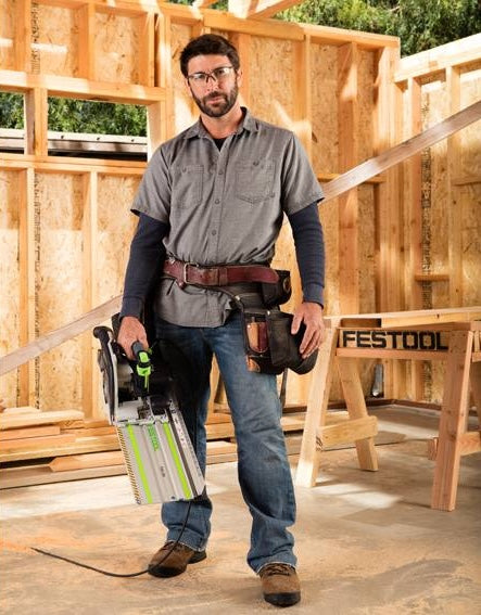 Man wearing workwear holding cordless carpentry saw in a wood-framed construction site with a Festool workbench nearby