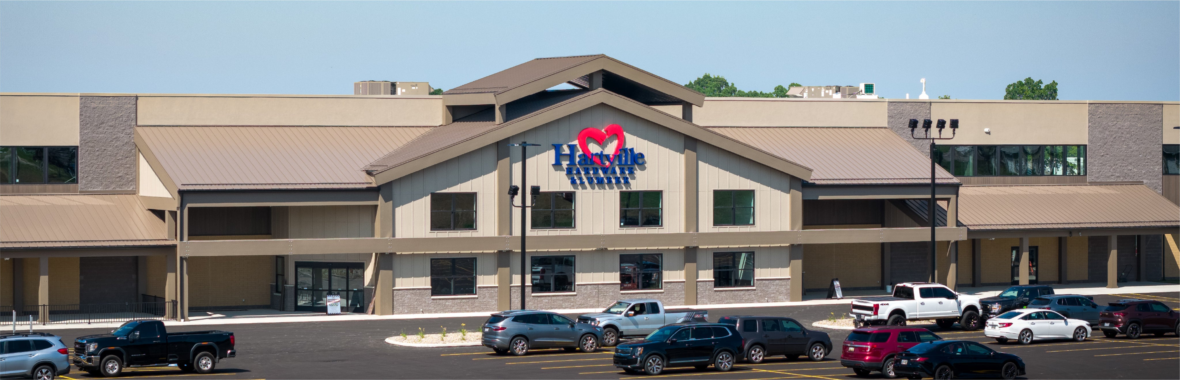 Wide exterior view of a Hartville Hardware store featuring a stone facade and large parking lot filled with vehicles under clear daylight sky