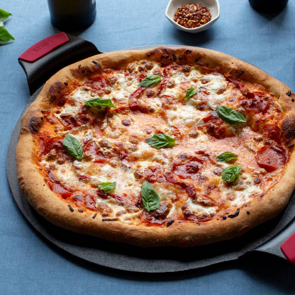 15-inch Lodge cast iron pizza pan with silicone grips holding a freshly baked pizza topped with basil leaves in Kitchenware collection