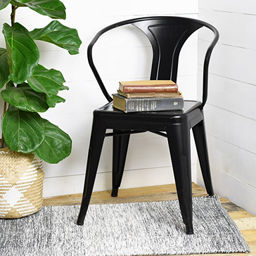 Black metal casual tin chair with curved backrest placed on rug and stacked books for home decor