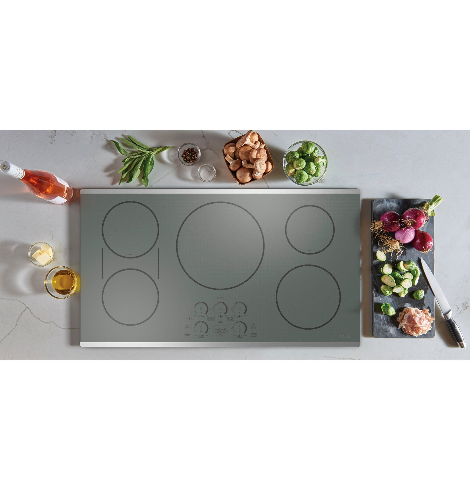 Top view of sleek 36-inch touch control induction cooktop with kitchen ingredients and cutting board nearby