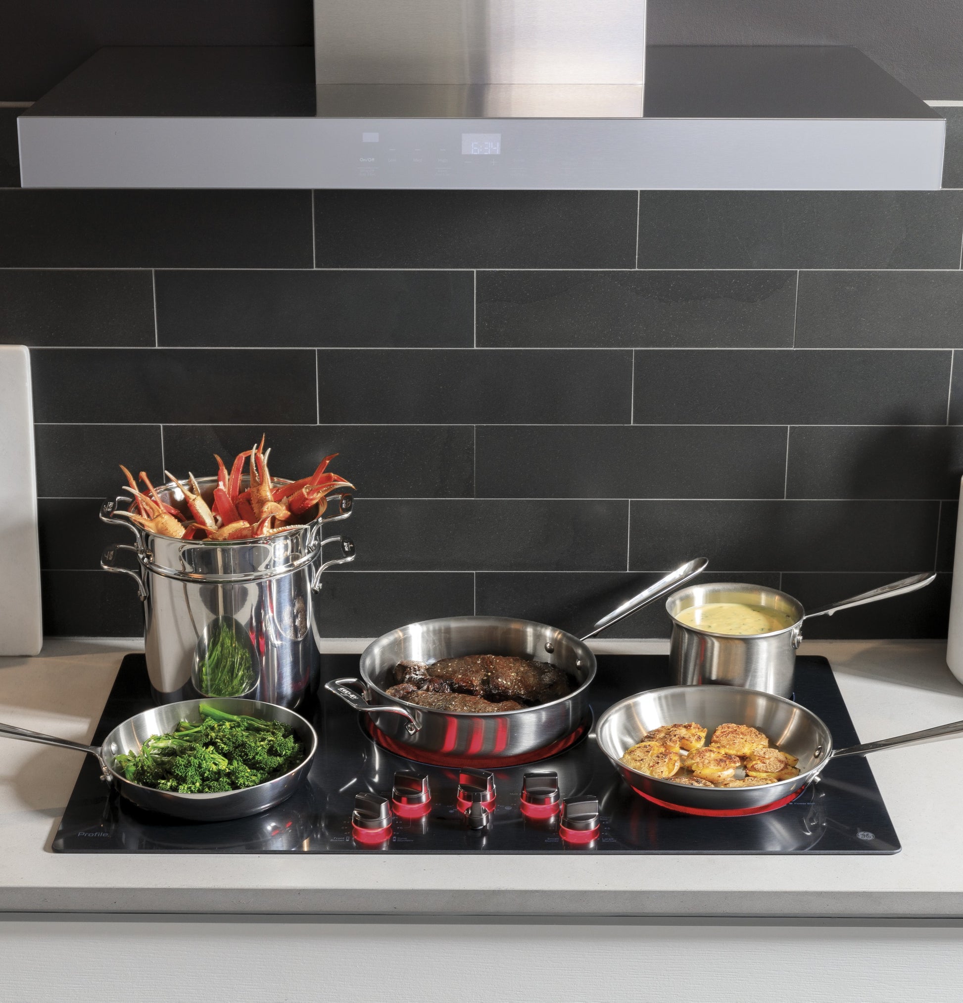 Contemporary kitchen scene with a stainless steel wall mount hood above a gas cooktop cooking various dishes, range hoods collection.