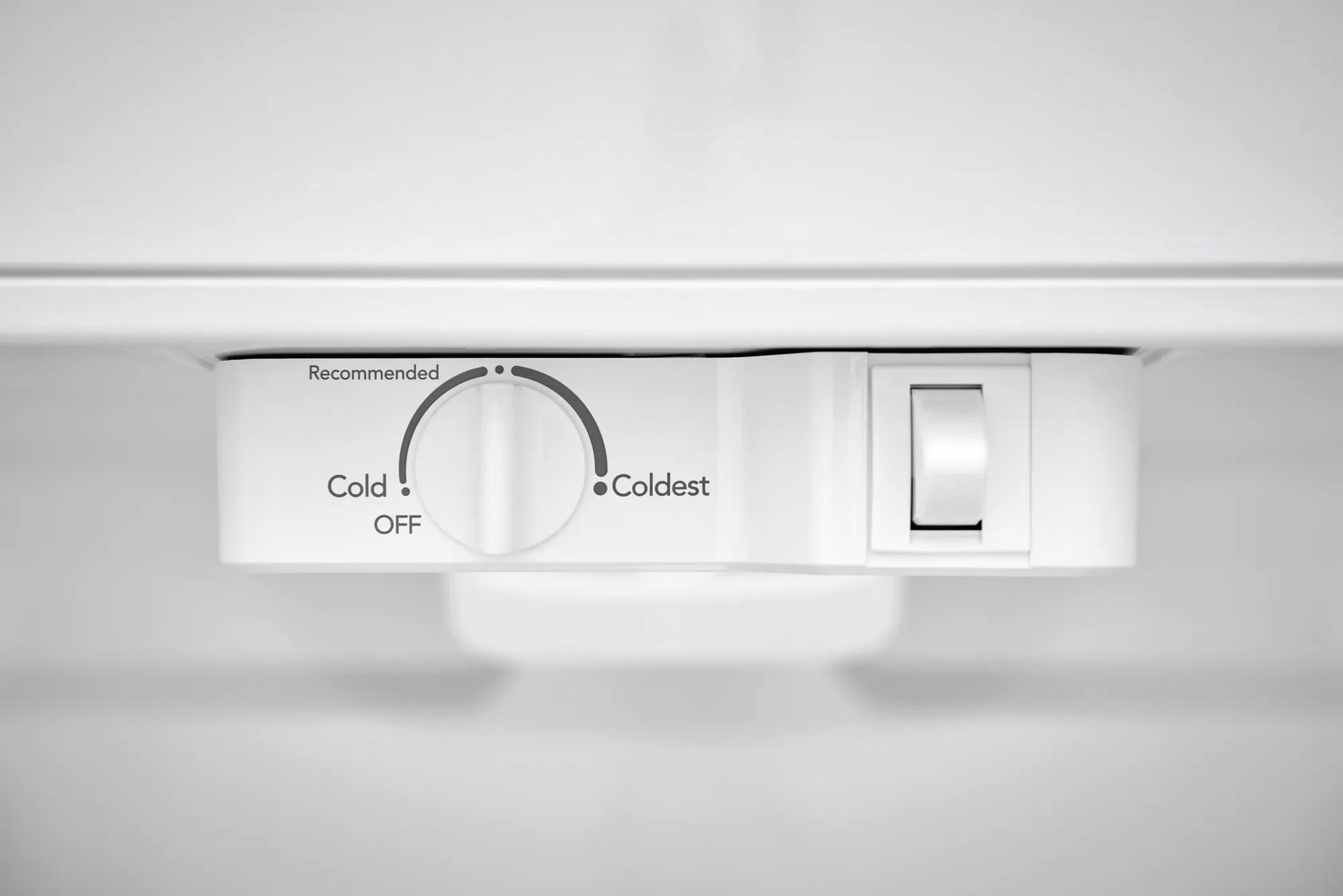 Close-up of white temperature control dial and light switch inside a top freezer refrigerator in Appliances collection