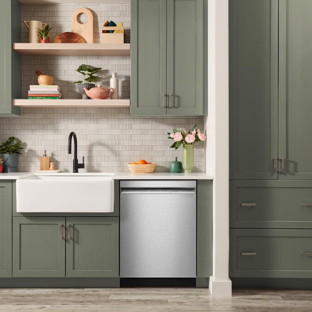 Stainless steel dishwasher installed under white countertop amid green cabinetry in modern kitchen with farmhouse sink