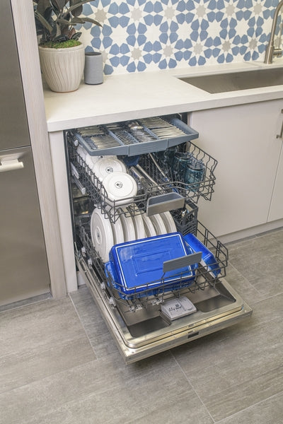 Open 24-inch custom panel ready dishwasher filled with clean white dishes and blue containers in modern kitchen design