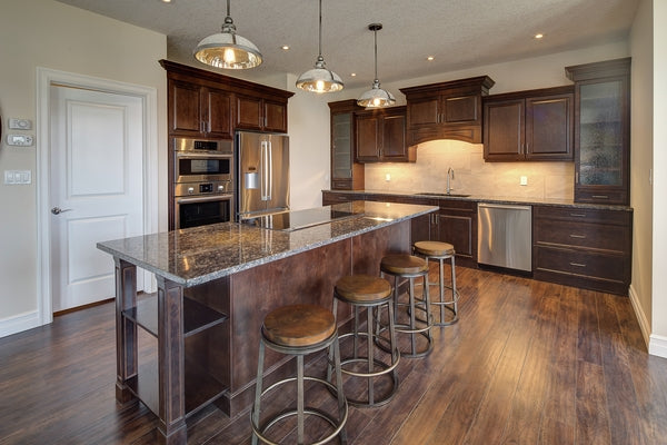 Modern kitchen with dark wood cabinets, stainless steel appliances, granite island, and pendant lighting over bar stools
