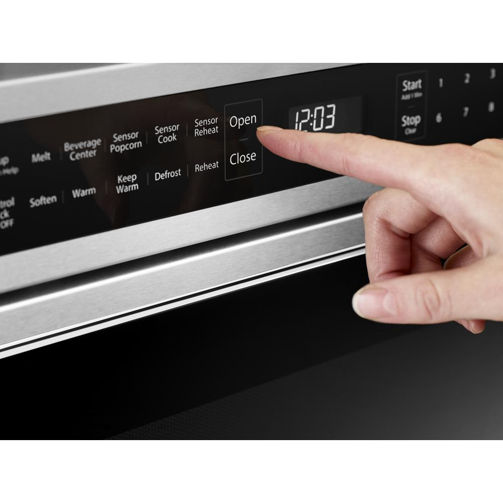 Close-up of stainless steel microwave drawer digital control panel with finger pressing open button from KitchenAid collection