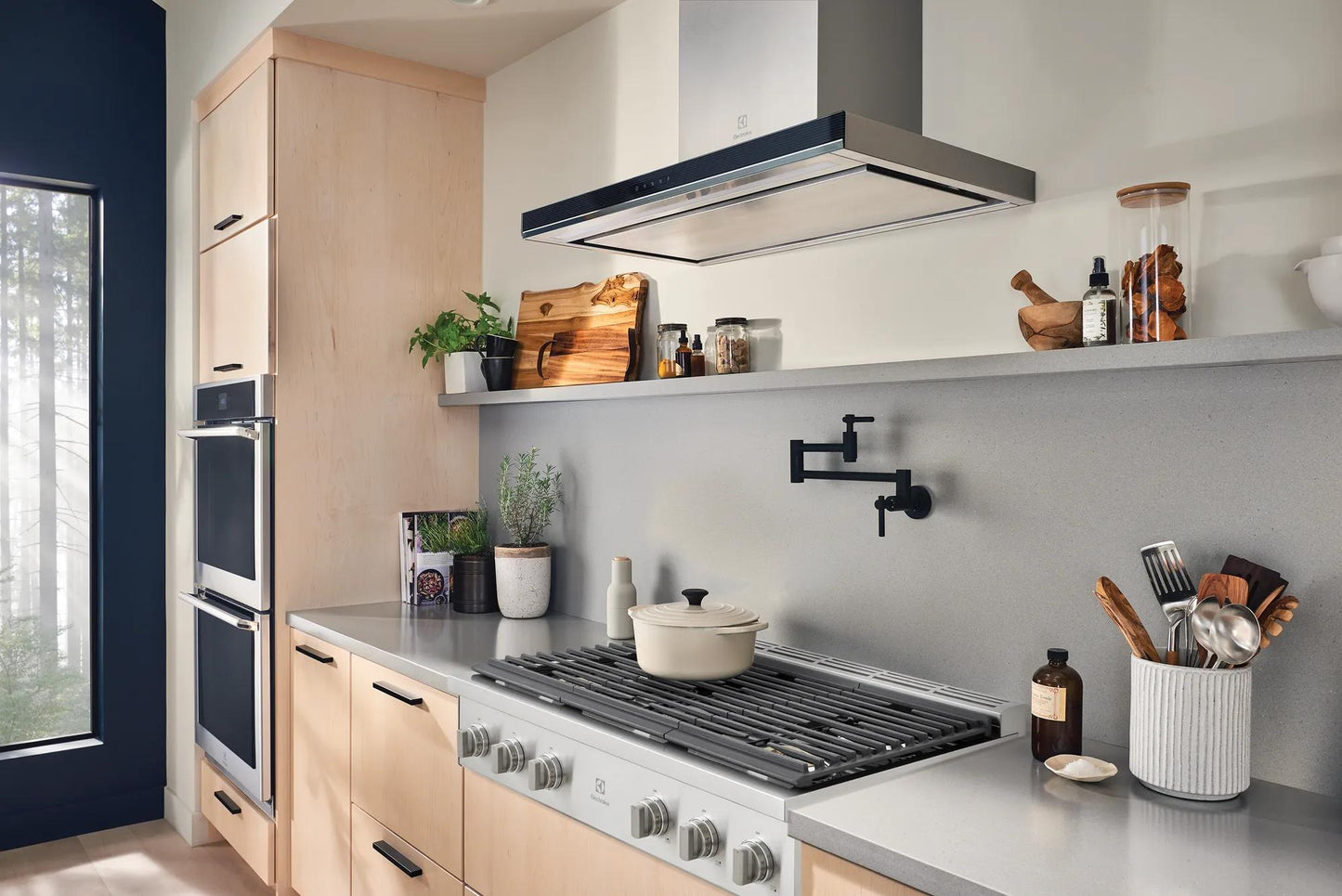 36-inch gas rangetop with brass burners and stainless steel controls in modern kitchen with light wooden cabinets and shelf