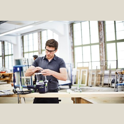 Man adjusting a Festool 576213 OF 1400 EQ-F-Plus router in a bright woodworking workshop setting