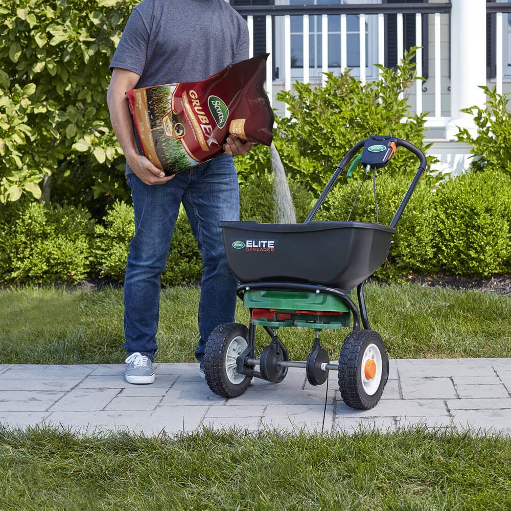 Person pouring grub killer granules into a lawn spreader for insect and pest control in garden care under $50 collections