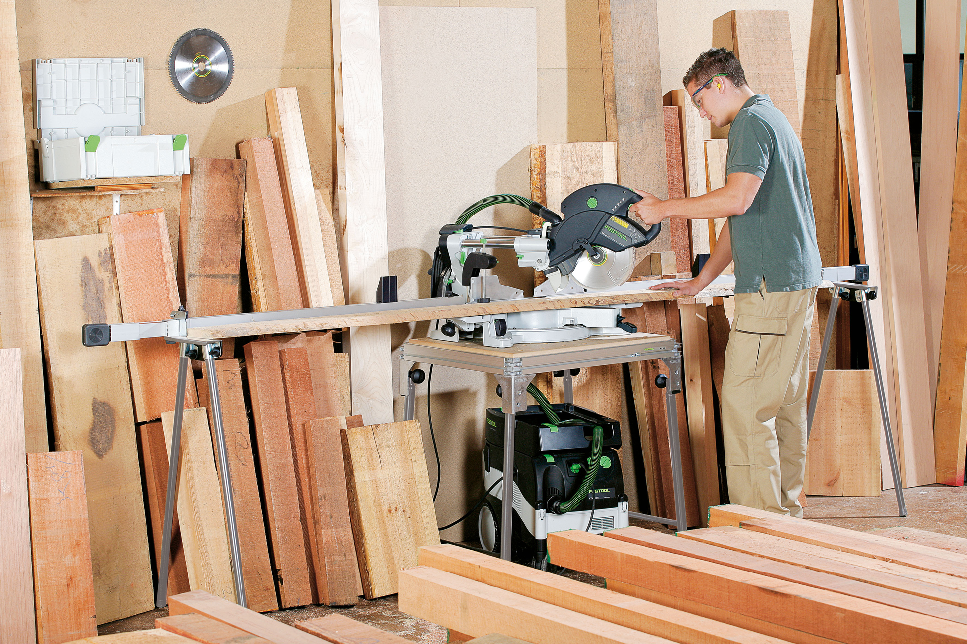 Person using Festool sliding compound miter saw to cut wood in workshop setting among power tools and saws collections