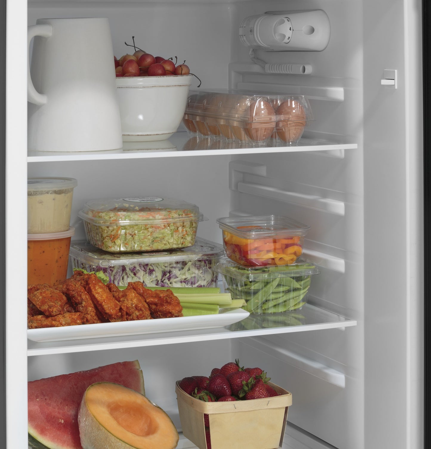 Interior view of a top-freezer refrigerator neatly stocked with fresh produce, prepared food, eggs, and beverages from Refrigerators collection