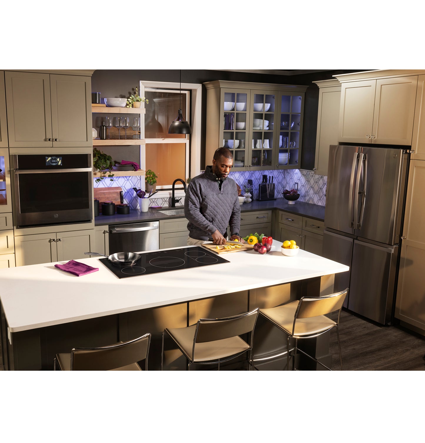 Modern kitchen with gray cabinetry and stainless appliances featuring a built-in induction cooktop on white island countertop