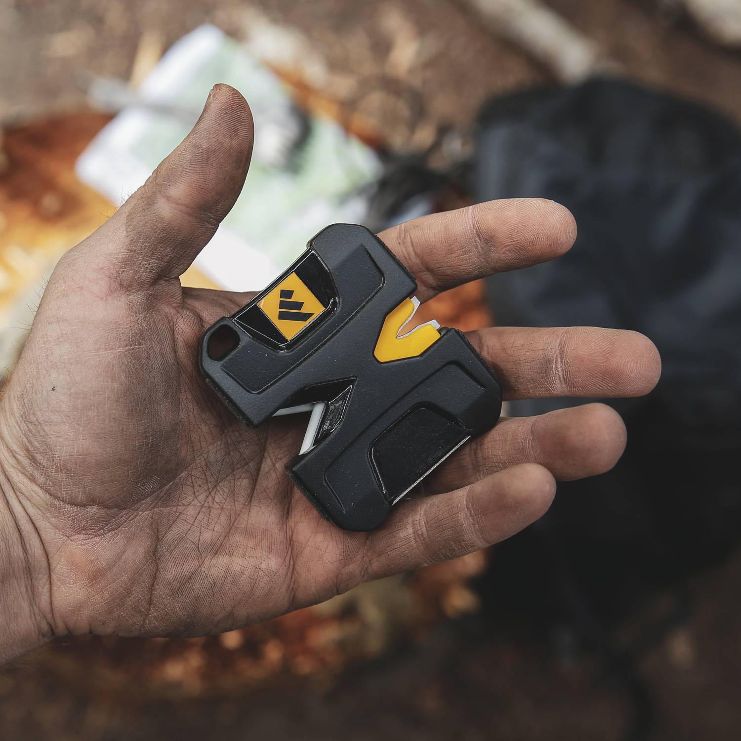 Hand holding compact black and yellow pivot knife sharpener for outdoor tools and home improvement use