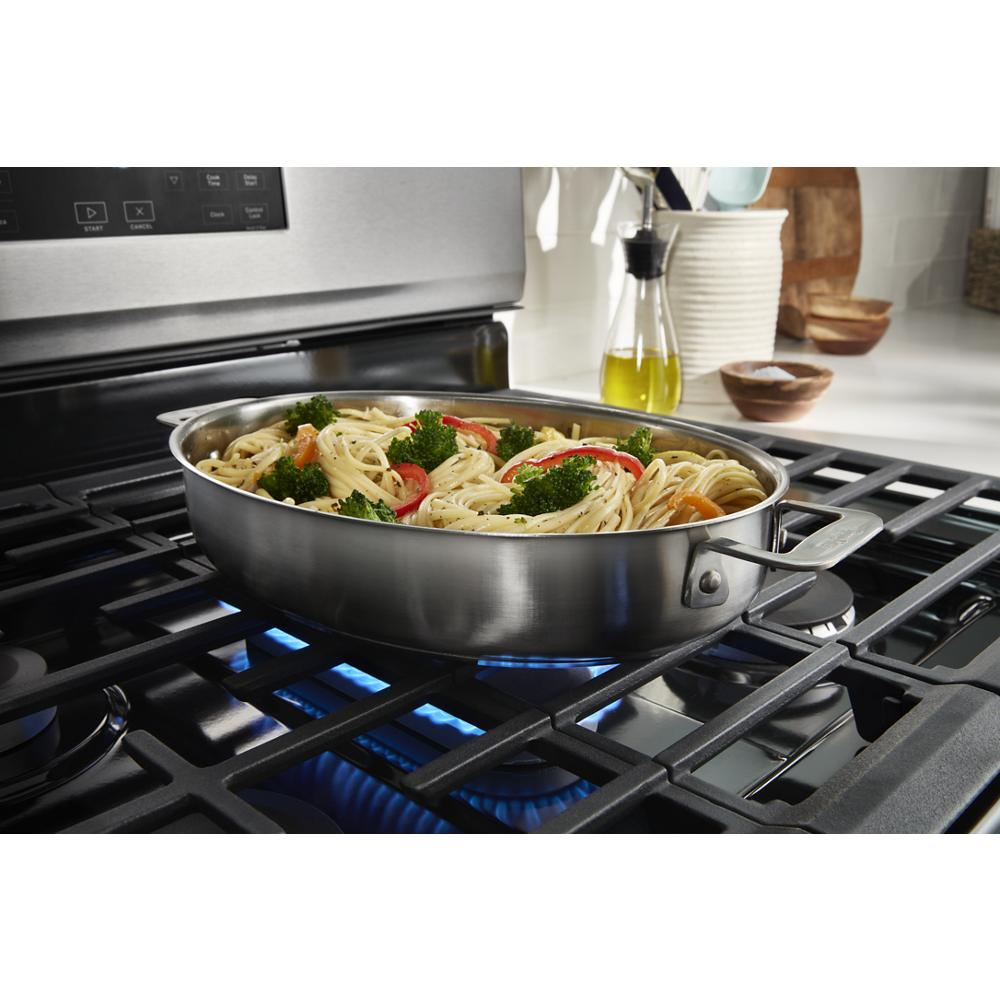 Stainless steel gas range burner with blue flame heating a skillet of pasta and vegetables in modern kitchen setting