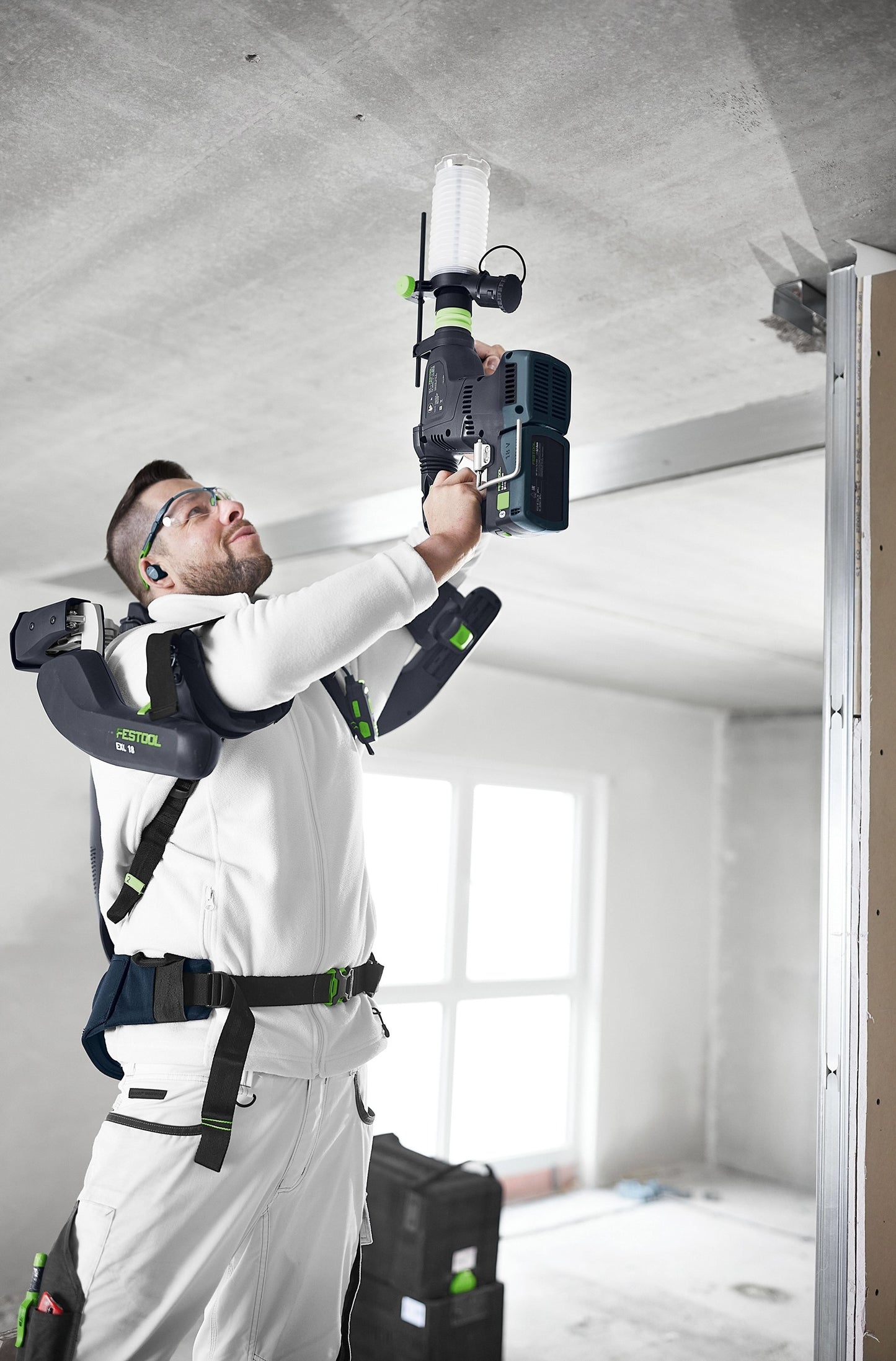 Construction worker using cordless drilling tool with attached dust extraction device on ceiling indoors
