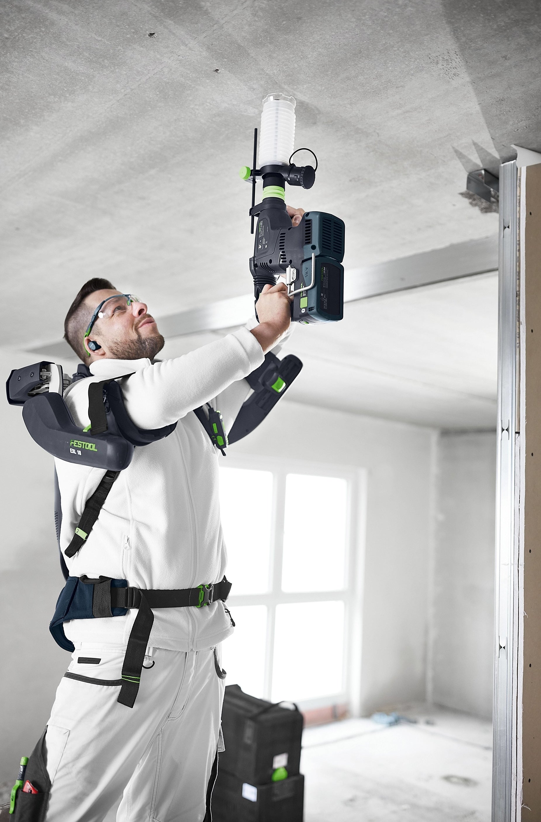 Construction worker using cordless drilling tool with attached dust extraction device on ceiling indoors