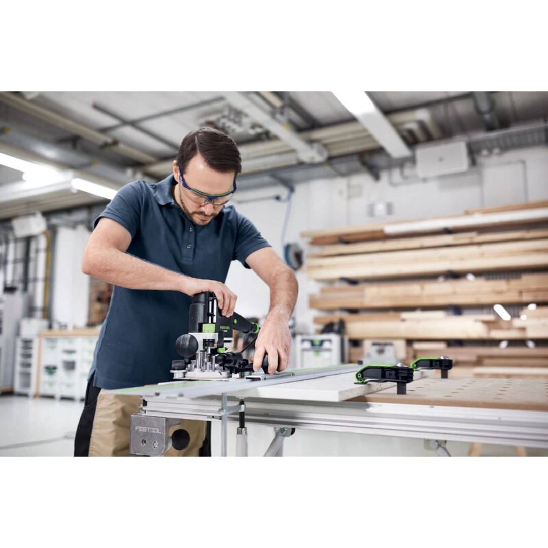 Man wearing safety glasses using a guide rail system with Festool router for precise woodworking tasks in workshop