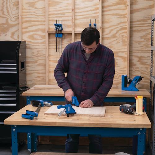 Man using blue woodworking clamps on hardwood bench top in tool accessories and home improvement workspace