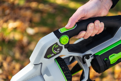 Close-up of hand holding cordless blower with black handle and green accents for outdoor home cleanup tasks