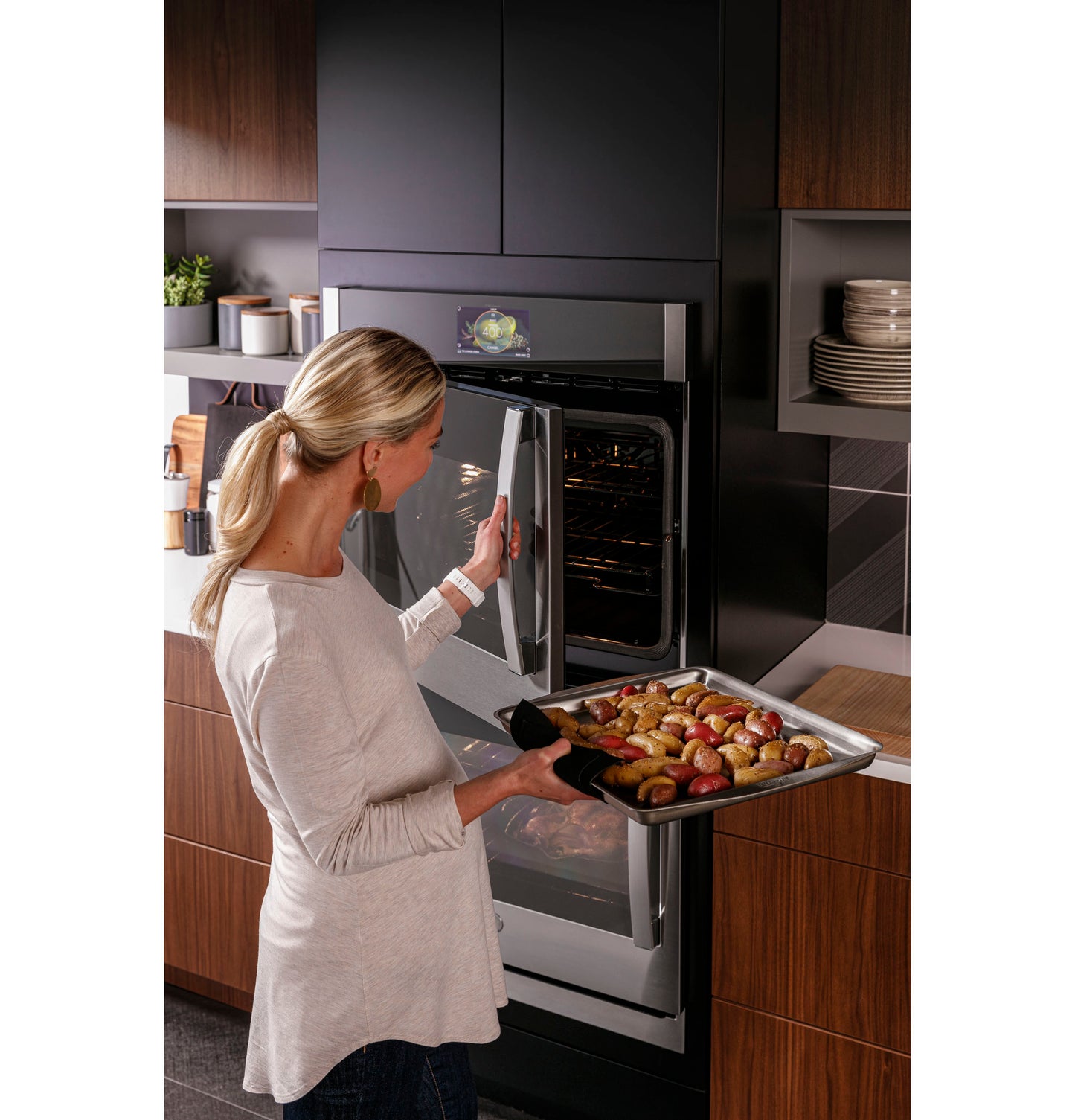 Woman removing roasted vegetables from stainless steel built-in double wall oven in modern kitchen setting