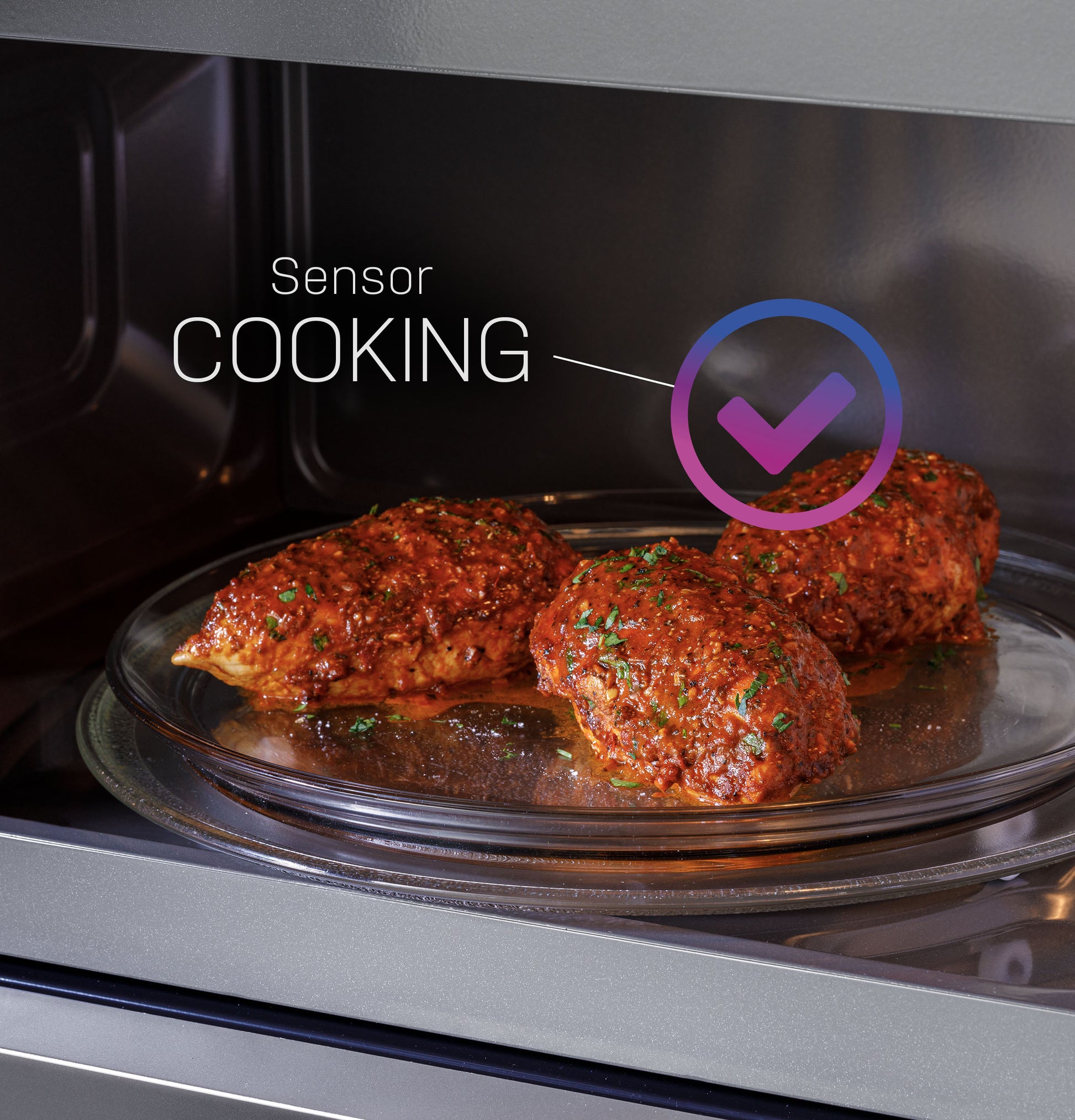 Close-up of seasoned chicken cooking on glass tray inside stainless steel microwave oven with sensor cooking feature icon visible