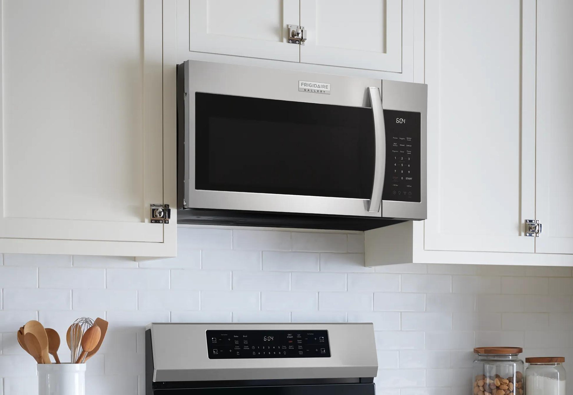 Stainless steel over-the-range microwave installed above stove in bright kitchen with white cabinets and backsplash