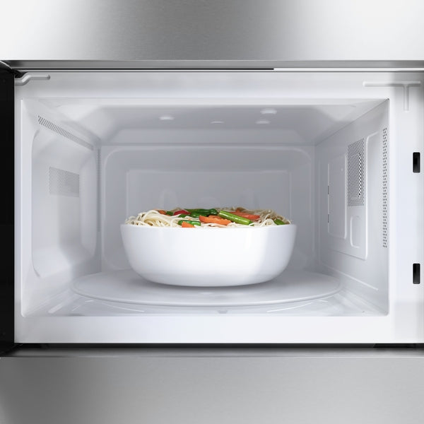 Interior view of stainless steel built-in Bosch microwave with a white bowl of vegetables and noodles on the turntable
