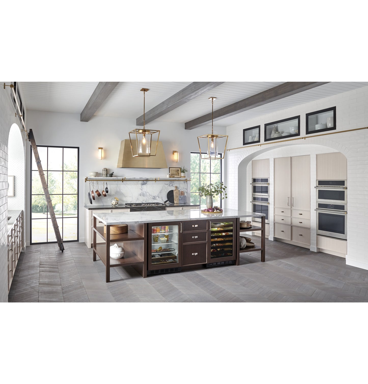Bright spacious kitchen with marble island, built-in ovens, glass-front beverage fridge, and natural light in appliances collection