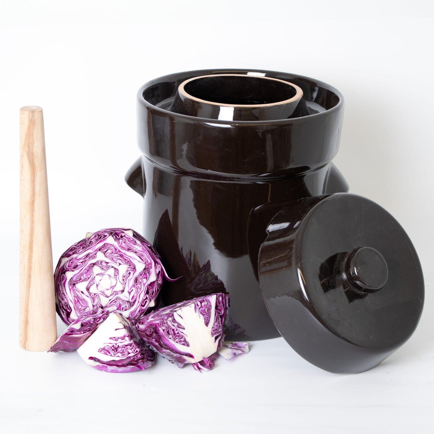 Glossy dark ceramic crock with lid, wooden stomper, and purple cabbage pieces for kitchenware collection under $100