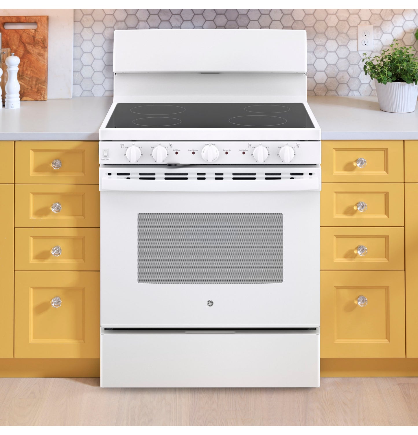 White free-standing electric radiant smooth cooktop range set in kitchen with yellow cabinetry and hex tile backsplash