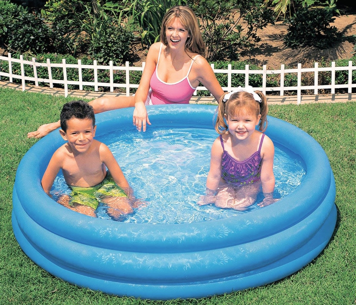 Adult and two children enjoying a small inflatable blue pool on grass in a backyard setting
