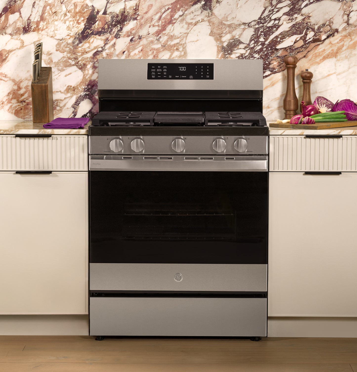 Stainless steel free-standing gas convection range with digital display and five control knobs in modern kitchen setting