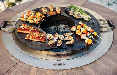 Round hot-rolled carbon steel griddle with handles cooking seafood and skewers on outdoor fire pit grill setup