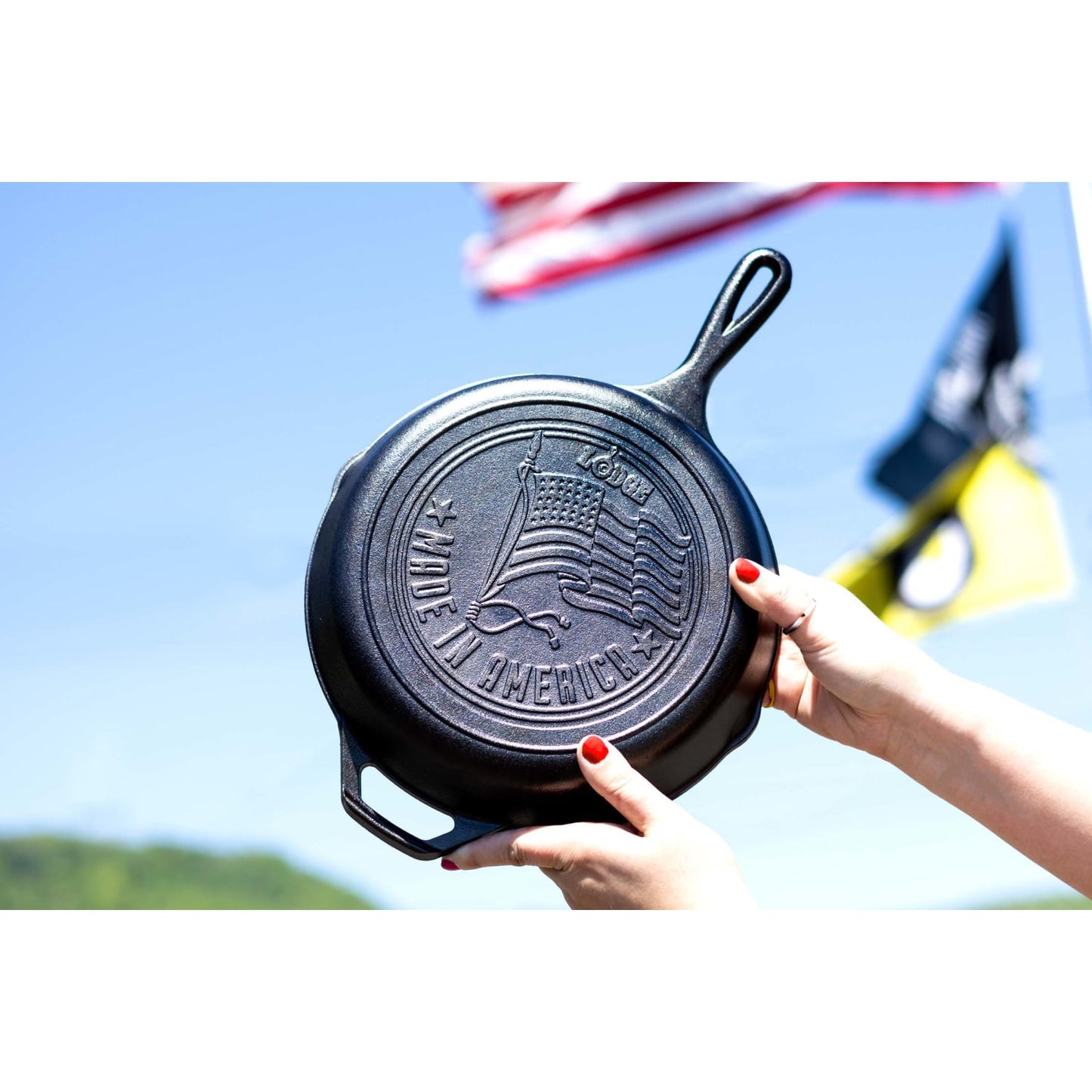 Hand holding Lodge cast iron skillet with embossed American flag and Made in America text outdoor background kitchenware product
