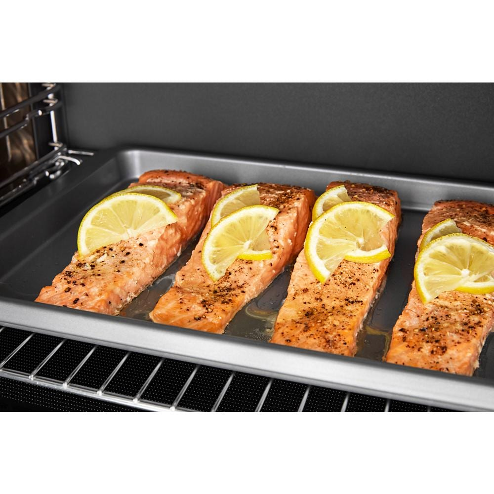 Four seasoned salmon fillets topped with lemon slices cooking on a tray inside a built-in microwave oven with air fry feature
