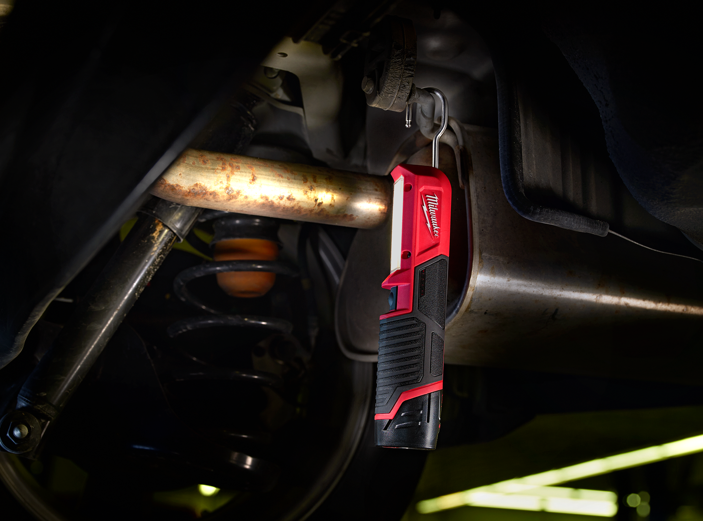 Compact red and black stick light hanging under vehicle exhaust pipe illuminating a dark workspace in tools collection