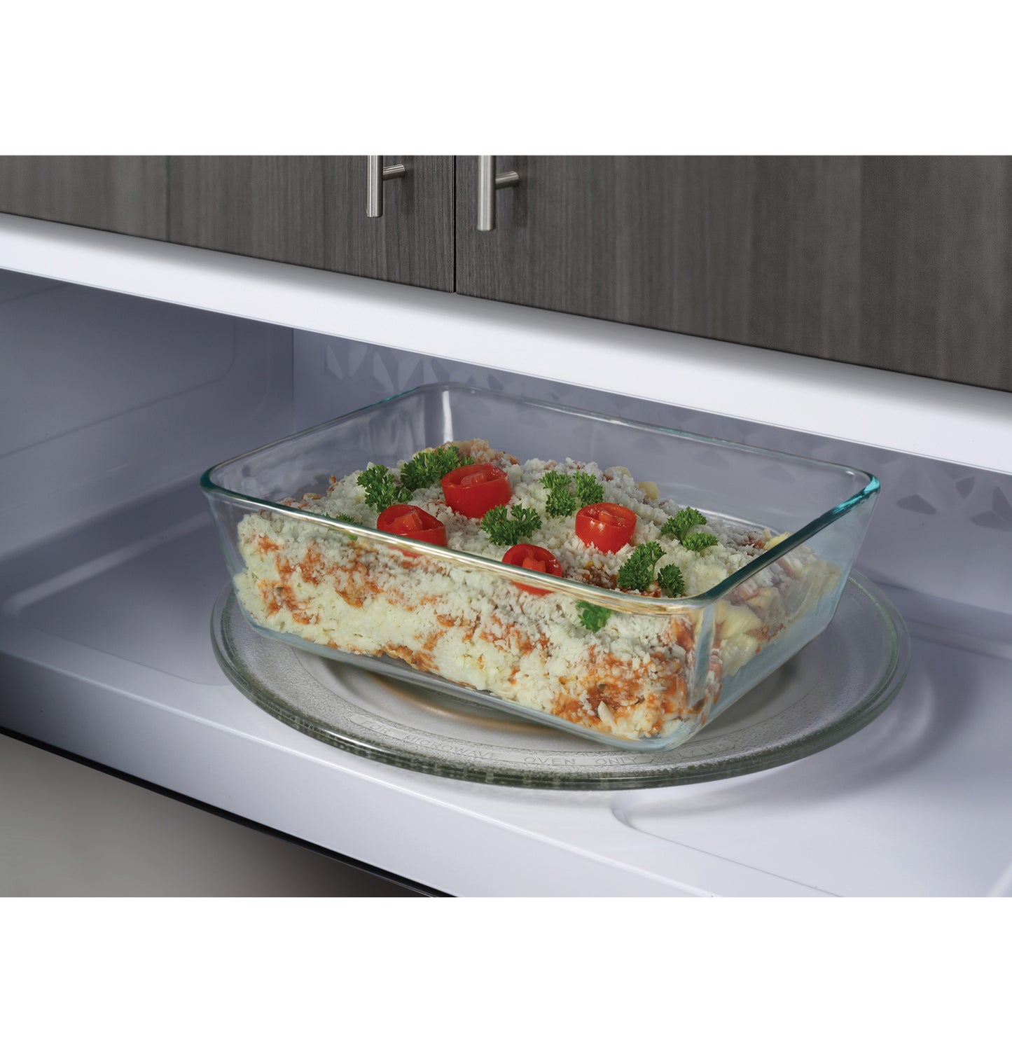 Glass casserole dish with baked pasta and garnish inside over-the-range microwave in kitchen appliances setting