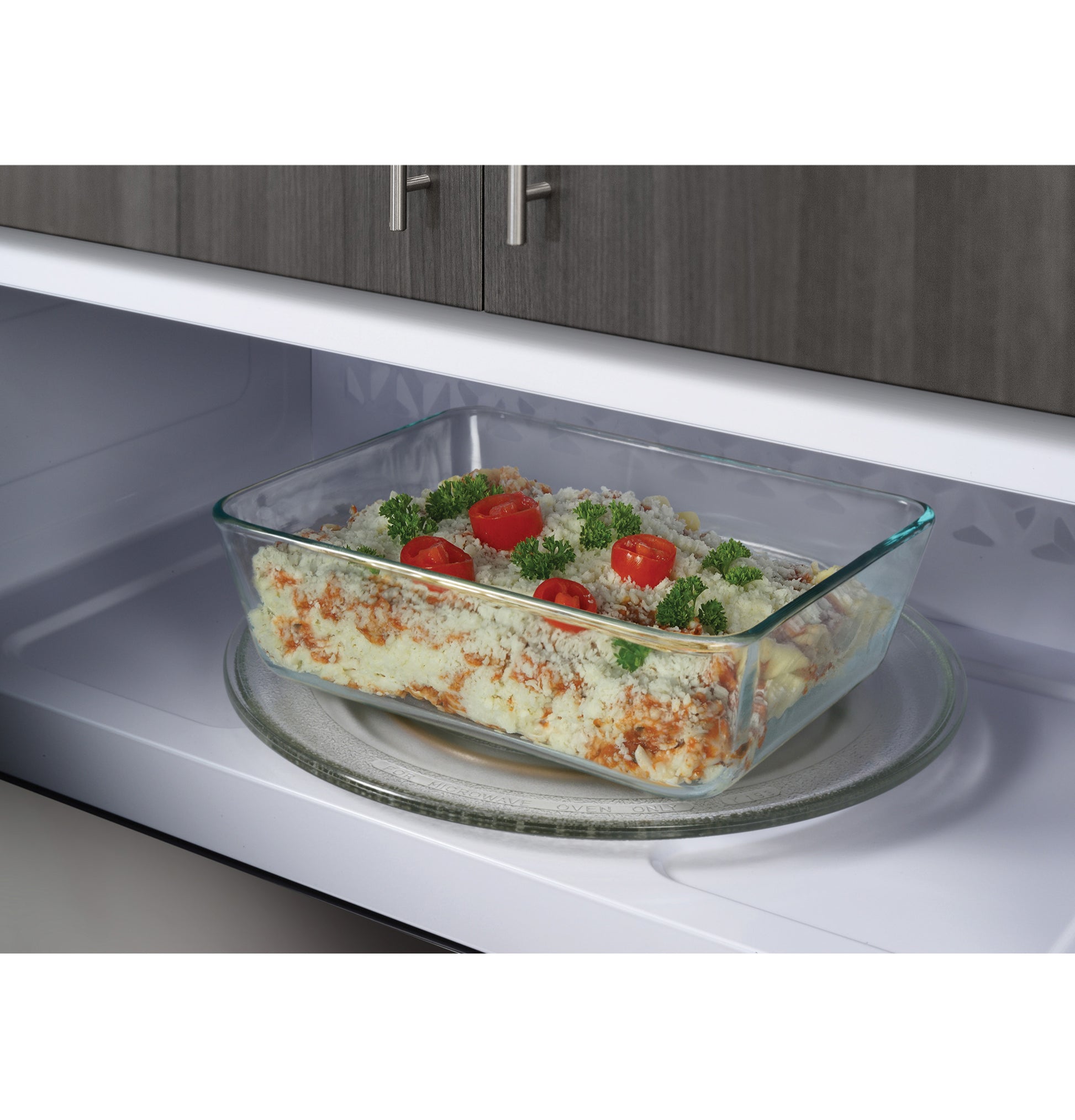 Glass casserole dish with baked pasta and garnish inside over-the-range microwave in kitchen appliances setting