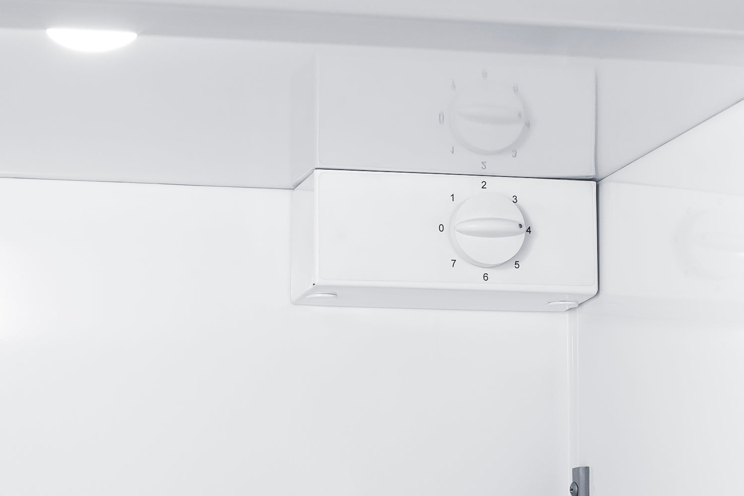 Close-up of white manual defrost freezer temperature control dial in appliance interior setting