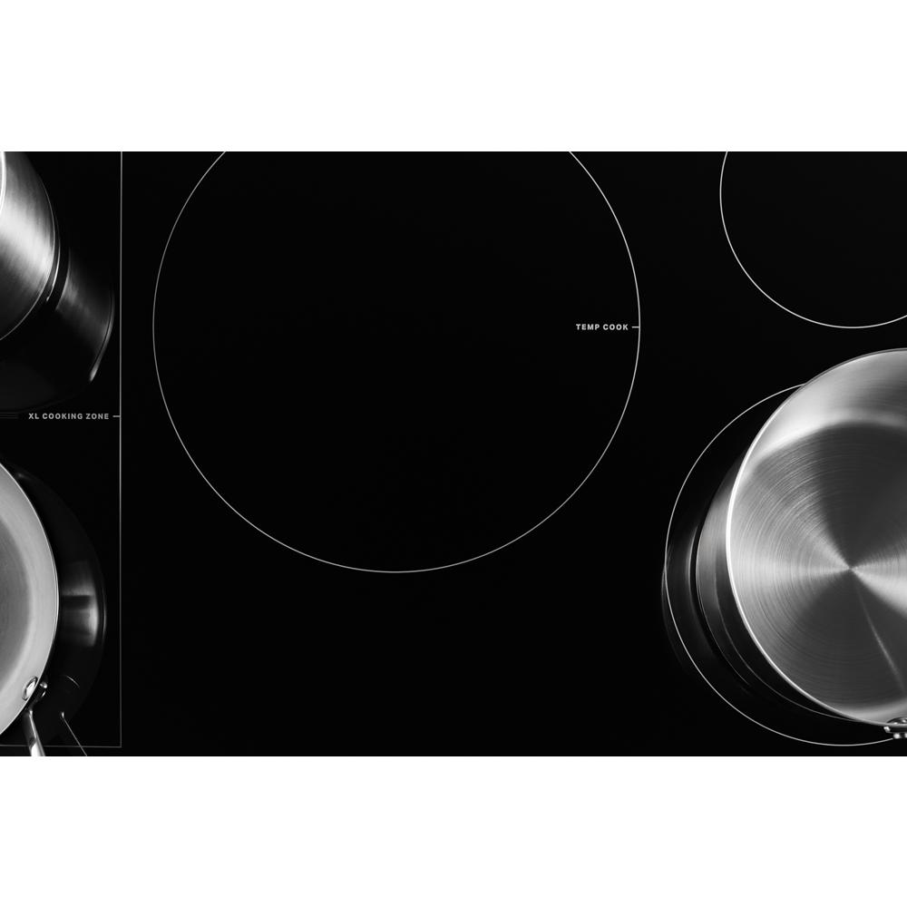 Black induction cooktop surface with XL cooking zone and stainless steel cookware in kitchen appliance setting